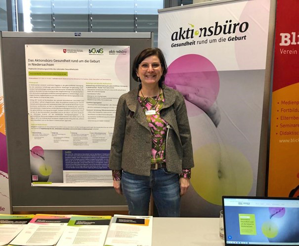 Sabine Scholz-de Wall vor dem Stand des Aktionsbüros mit Projekt-Banner und -Poster