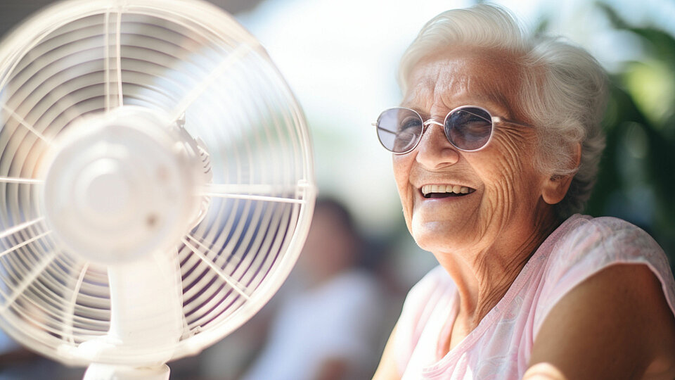 Eine ältere Frau bei warmen Wetter vor einem Standventilator