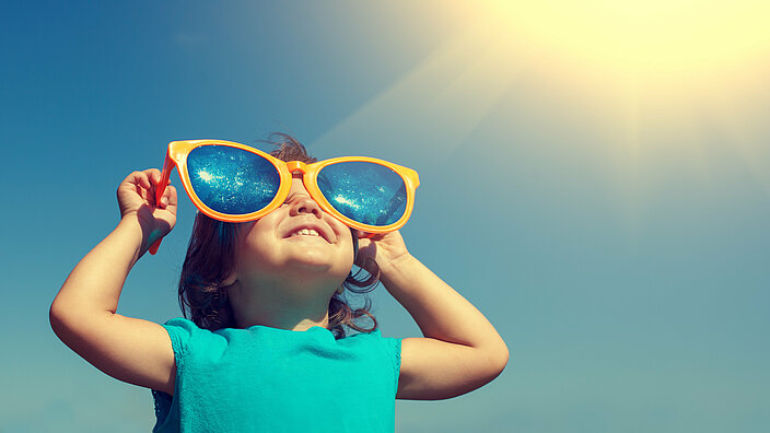 Kind schaut durch eine Sonnenbrille in die Sonne
