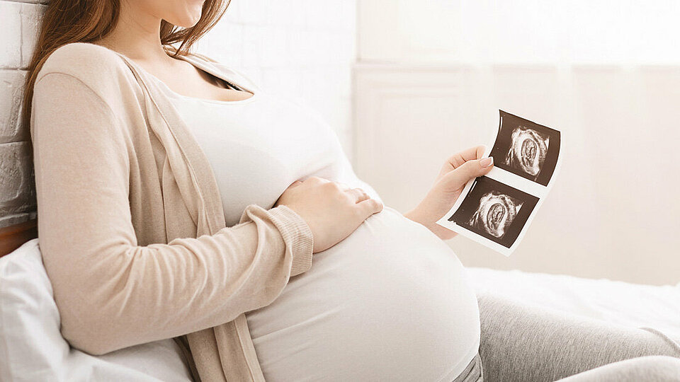 Schwangere Frau hält Ultraschallbild im Bett liegend.