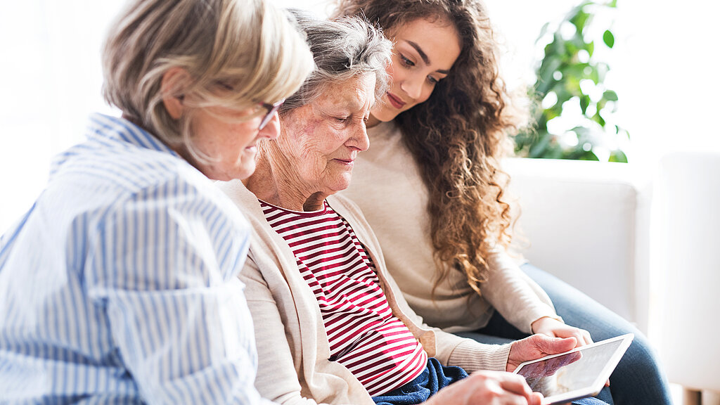 Mädchen und Mutter und Oma sitzen mit einem Tablet auf Sofa