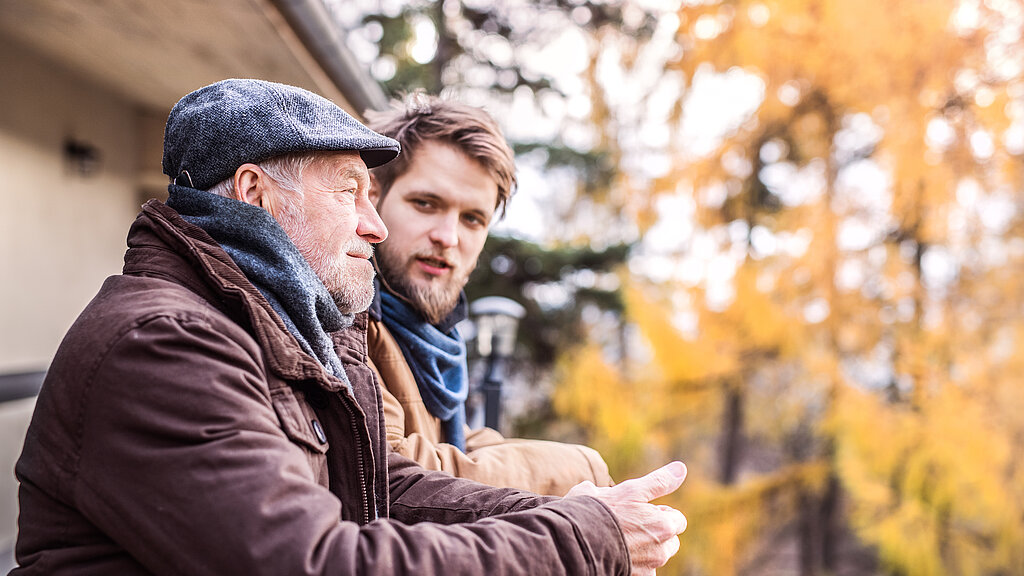 Älterer Mann und junger Mann sprechen draussen unter Herbstbäumen