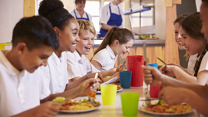Eine Gruppe von fröhlichen Kindern sitzt am Tisch und isst.
