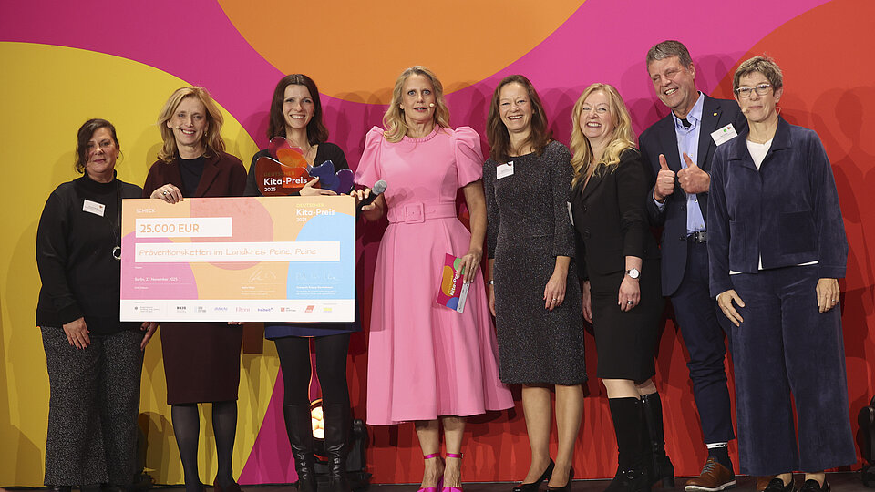 8 Personen vor einer bunten Wand halten einen großen Scheck in der Hand