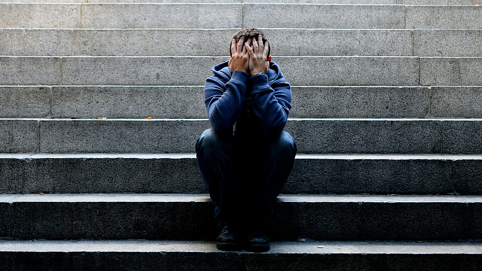 Ein Mann sitzt mit über den Kopf zusammengeschlagenen Händen auf einer Treppe