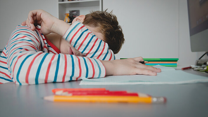 Ein Schüler schlägt bei den Hausaufgaben erschöpft die Hände über den Kopf