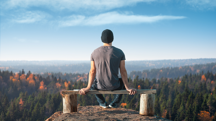 Ein Mann sitzt auf einem Aussichtspunkt über dem Wald. Rückansicht.